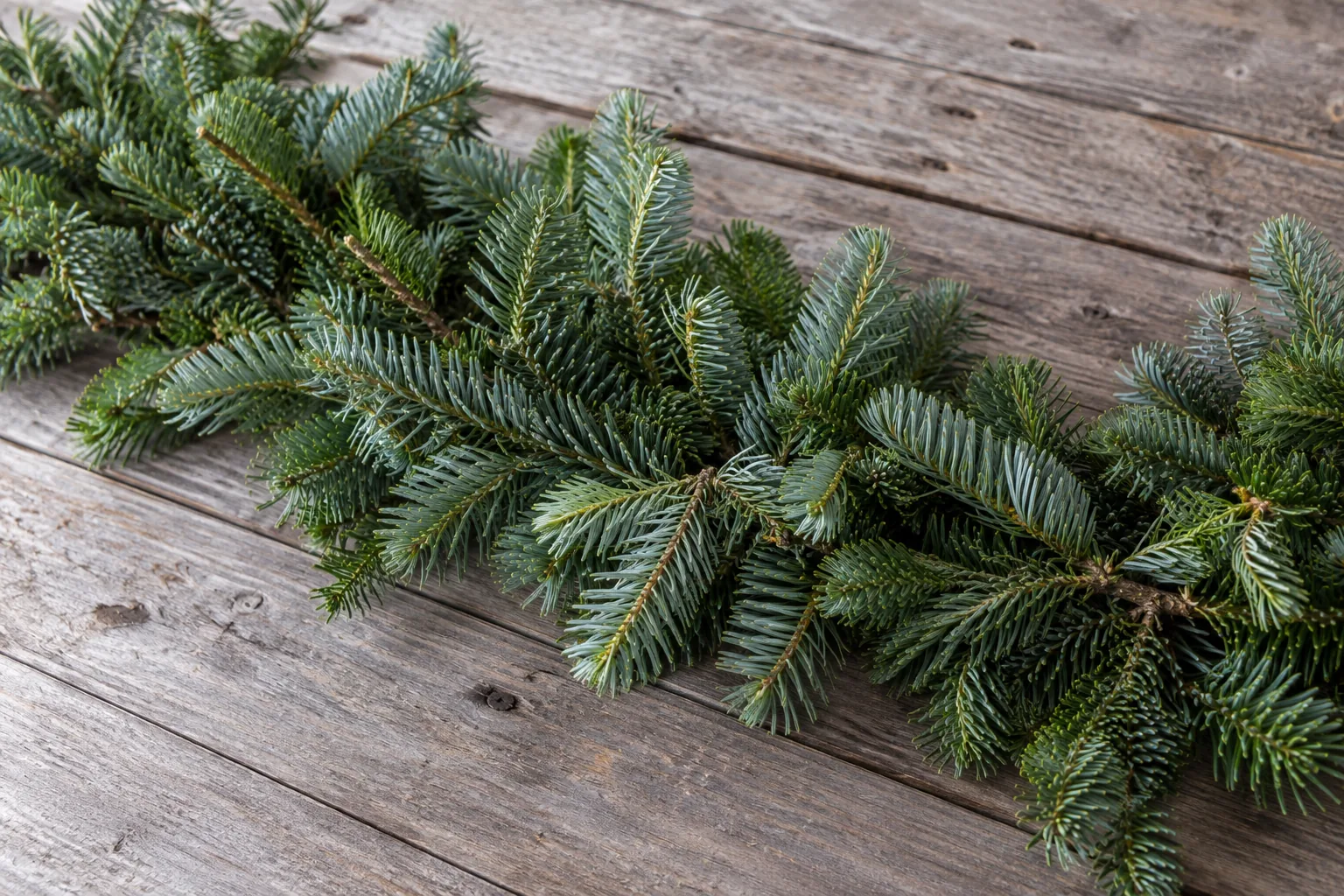 Fresh evergreen branches and garland resting on a weathered wood work surface.